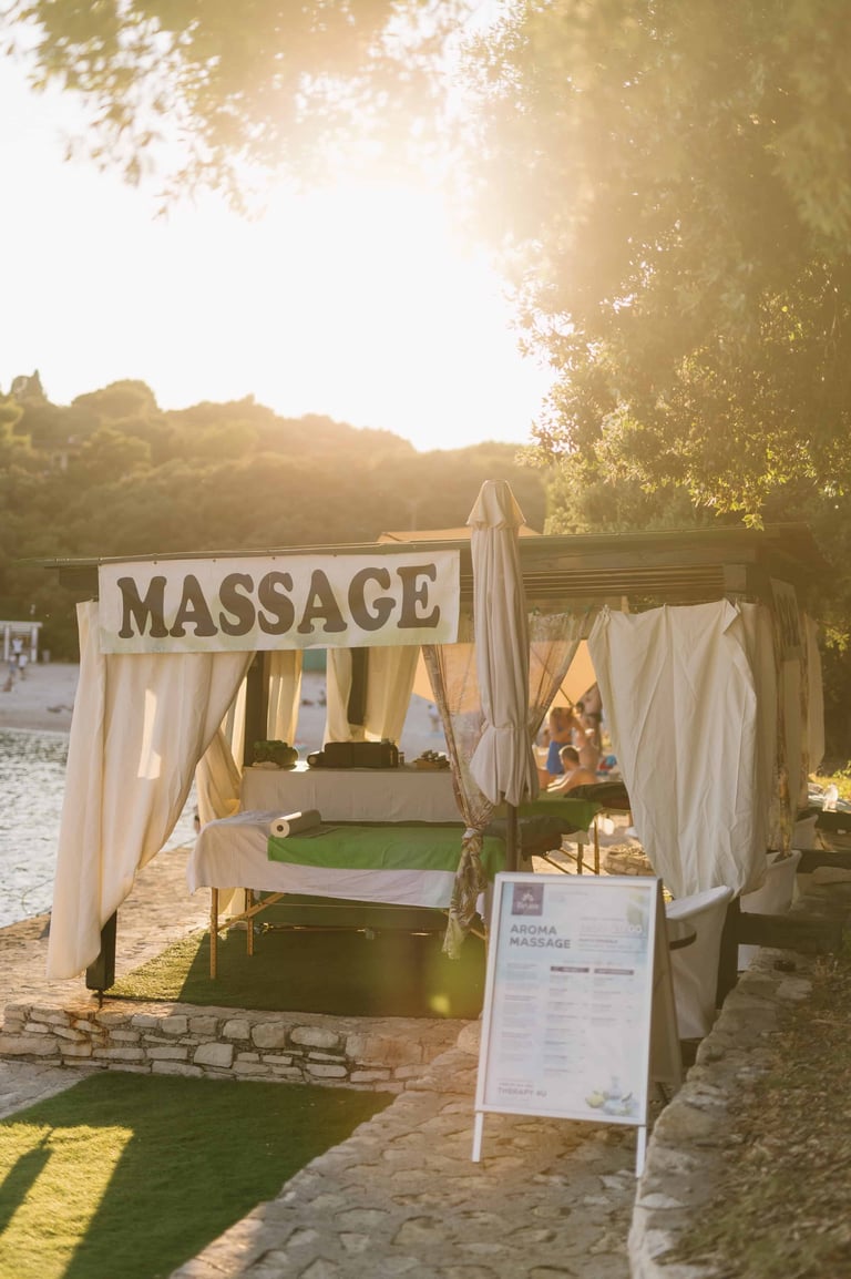 Outdoor massage pavilion with white draped curtains and green turf flooring at sunset by a waterside location