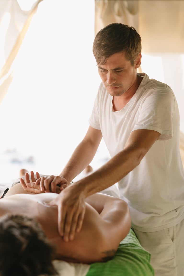 Male massage therapist performing a back massage on a client lying face down on a treatment table