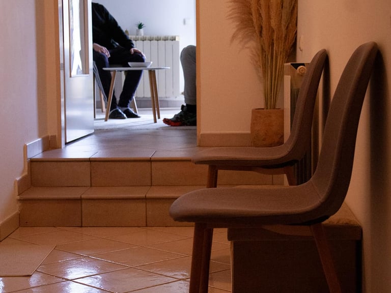 Modern wooden chairs in foreground with view through doorway to person sitting at desk in background office space