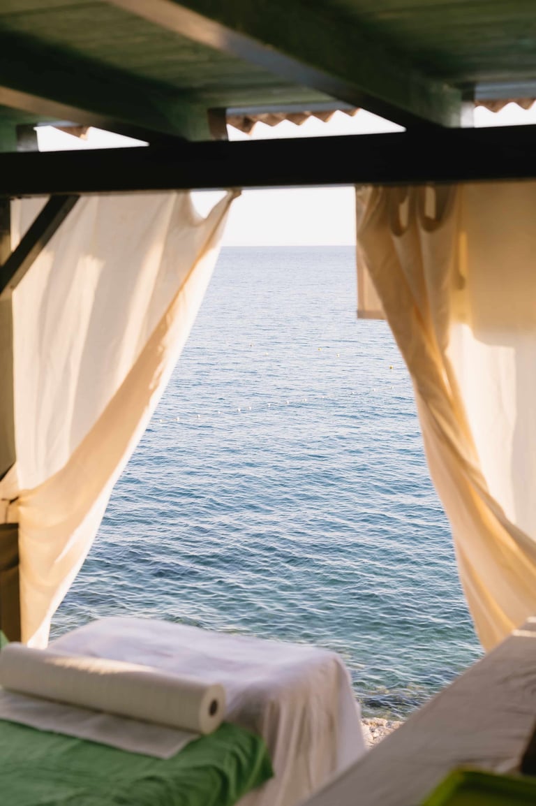 Oceanview from beachside cabana with white curtains framing calm blue sea and sandy beach below