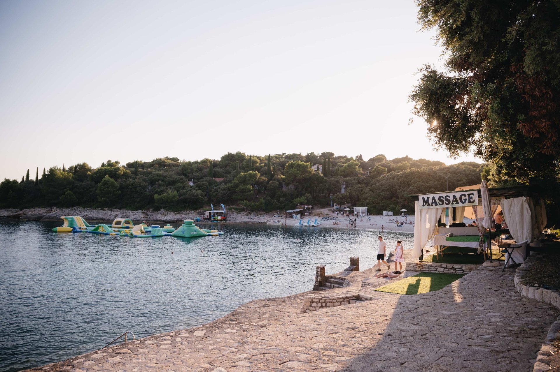 Beach cove with a massage tent, moored boats, and tree-covered hillside in the background